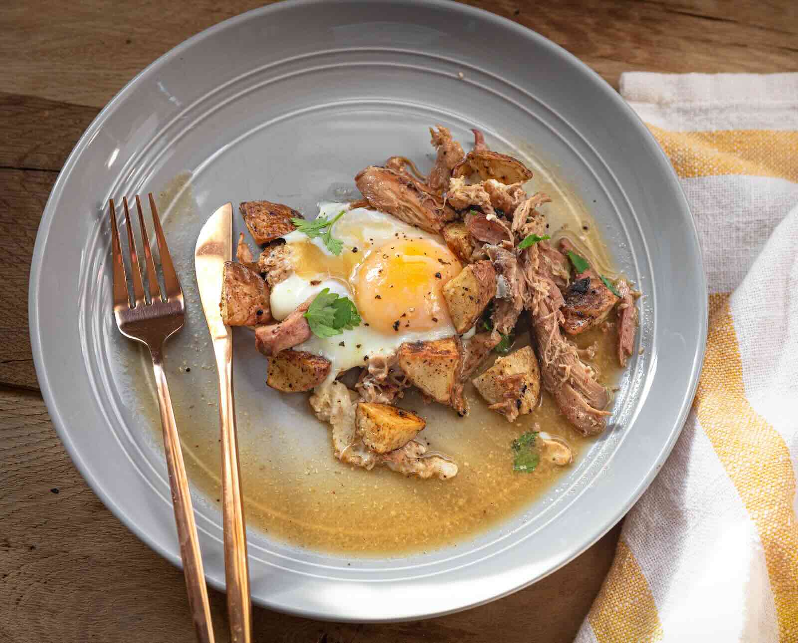 A serving of corned pheasant hash with a fried egg on a white plate with silverware