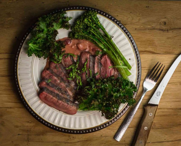 Sous vide cooked coose breast sliced on a plate with green garnish and a cherry sauce