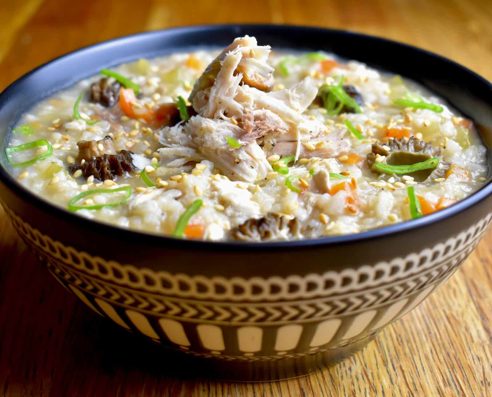 A bowl of rice porridge, garnished with celery, carrot, and scallions, served in a patterned blue bowl on a wooden surface
