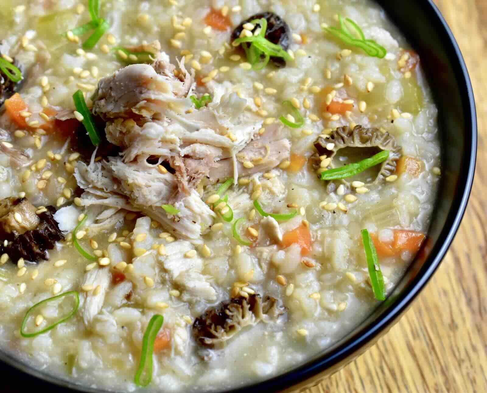 A close-up image of rice porridge with grouse meat, morel mushrooms, carrot, celery, and a scallion garnish
