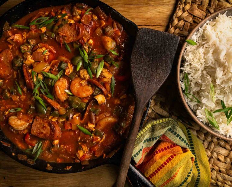 Upland bird jambalaya served in a cast iron skillet with a bowl of white rice and garnishes