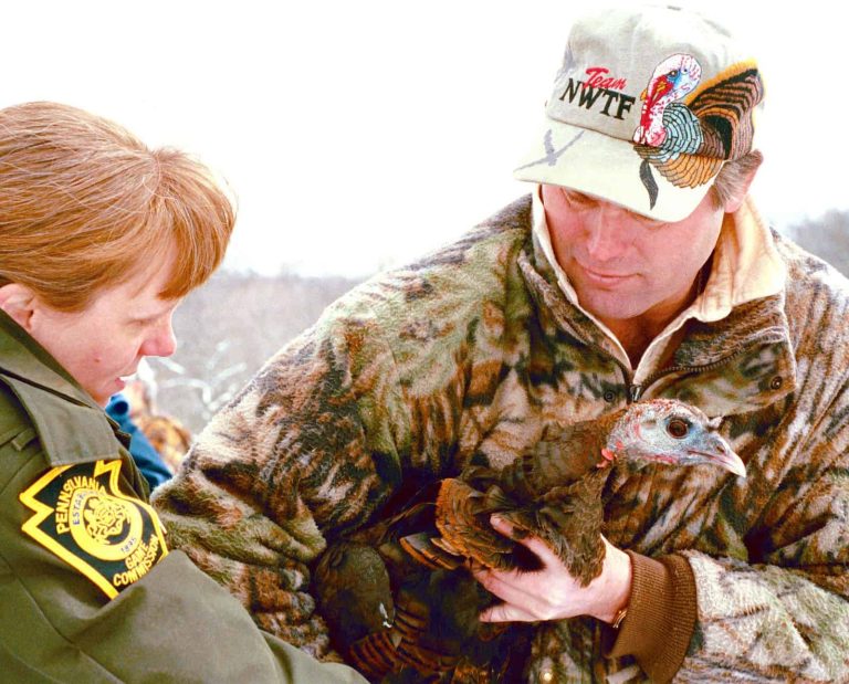 A National Wild Turkey Federation member holds a wild turkey next to a Pennsylvania Game Commission officer.