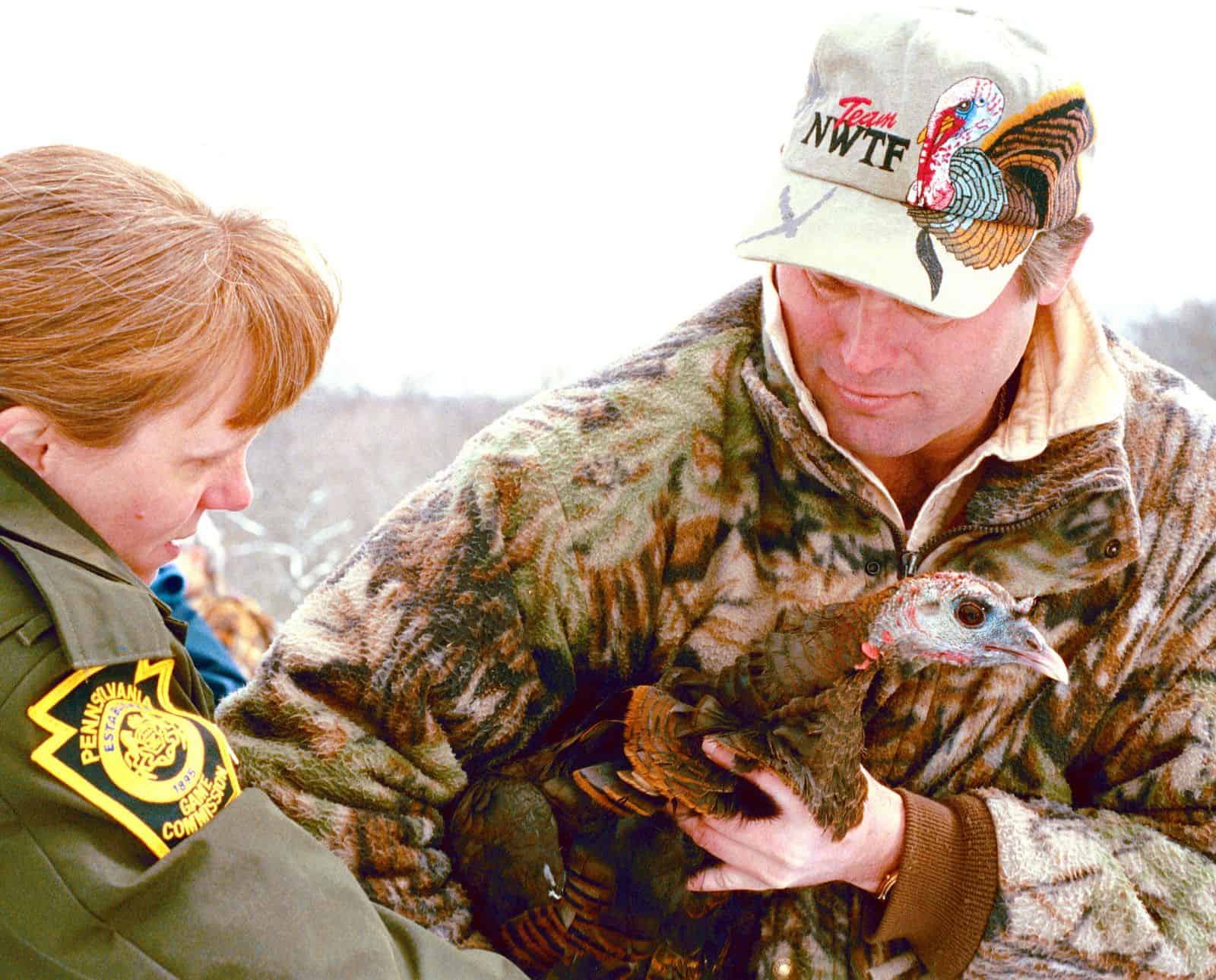 A National Wild Turkey Federation member holds a wild turkey next to a Pennsylvania Game Commission officer.