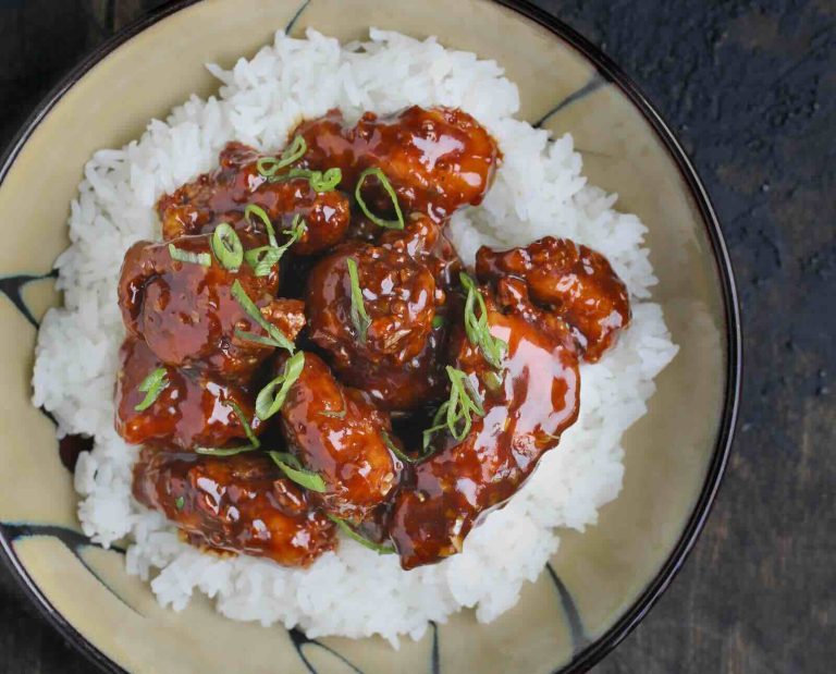 A serving of fried turkey breast in a Chinese orange sauce, topped with green onions and sesame seeds, served atop white rice on a plate