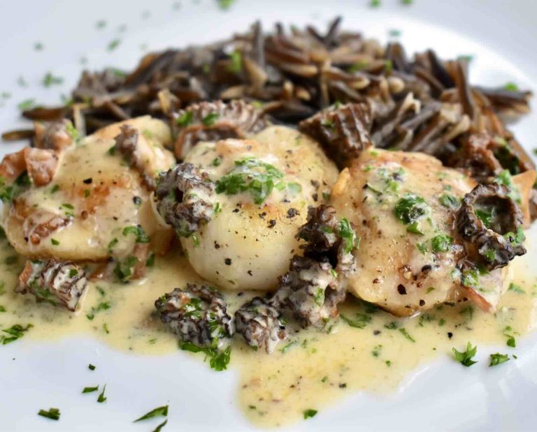 Three walleye cheeks in a creamy sauce, served alongside wild rice, on a white plate.