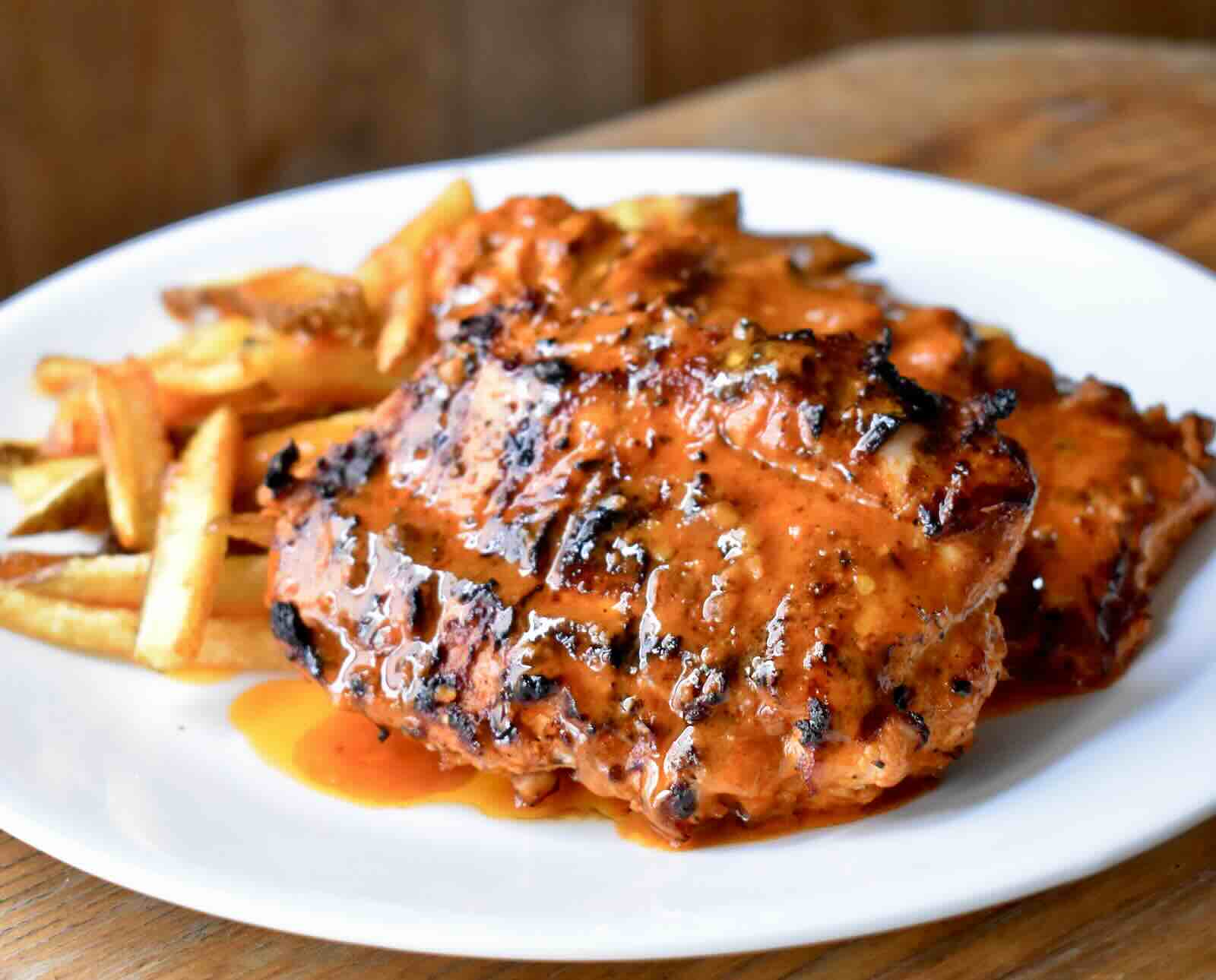 Turkey breast covered in a vibrant orange sauce, served with French fries on a white plate