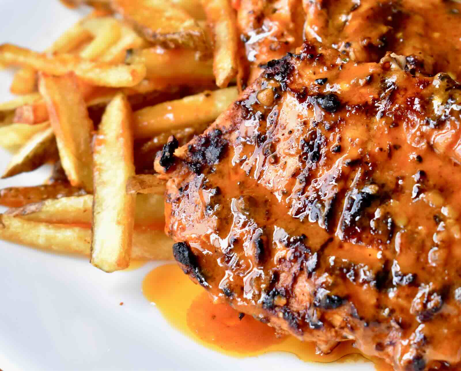 Turkey breast covered in a vibrant orange sauce, served with French fries on a white plate
