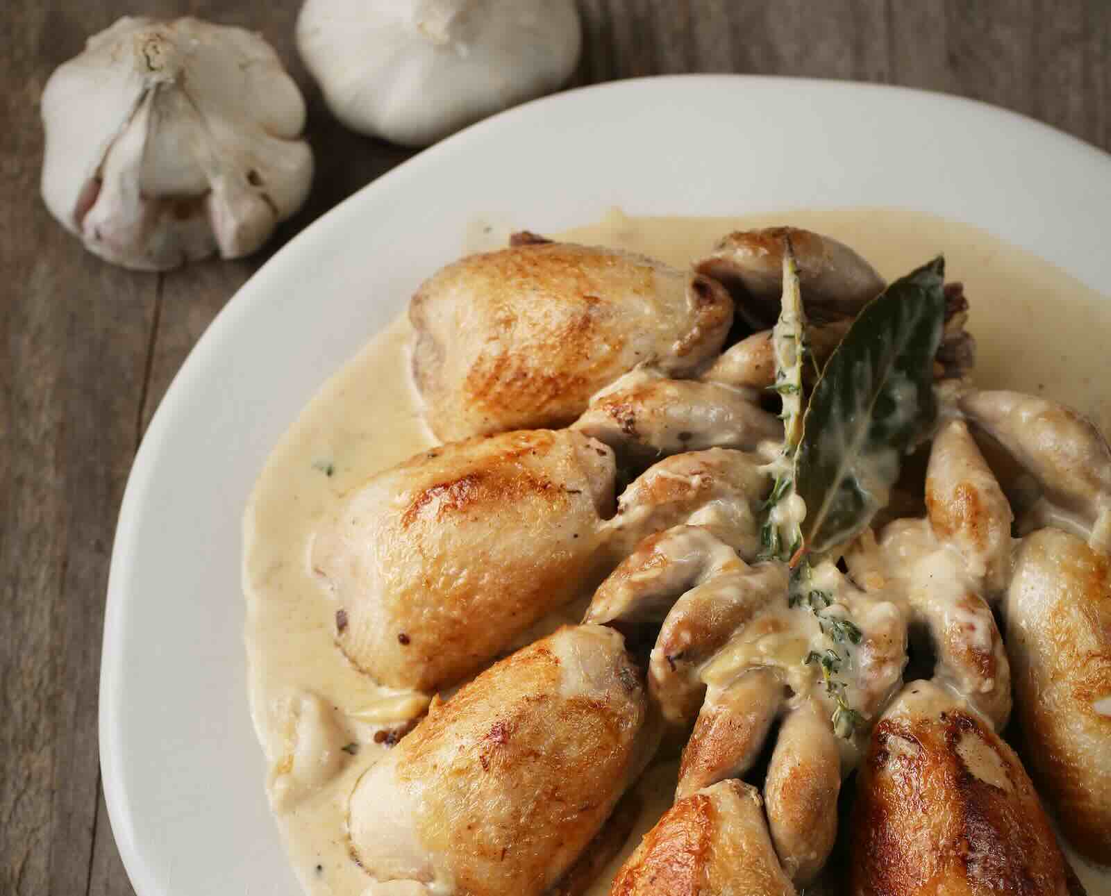 Roasted quail in a creamy garlic sauce on a white plate