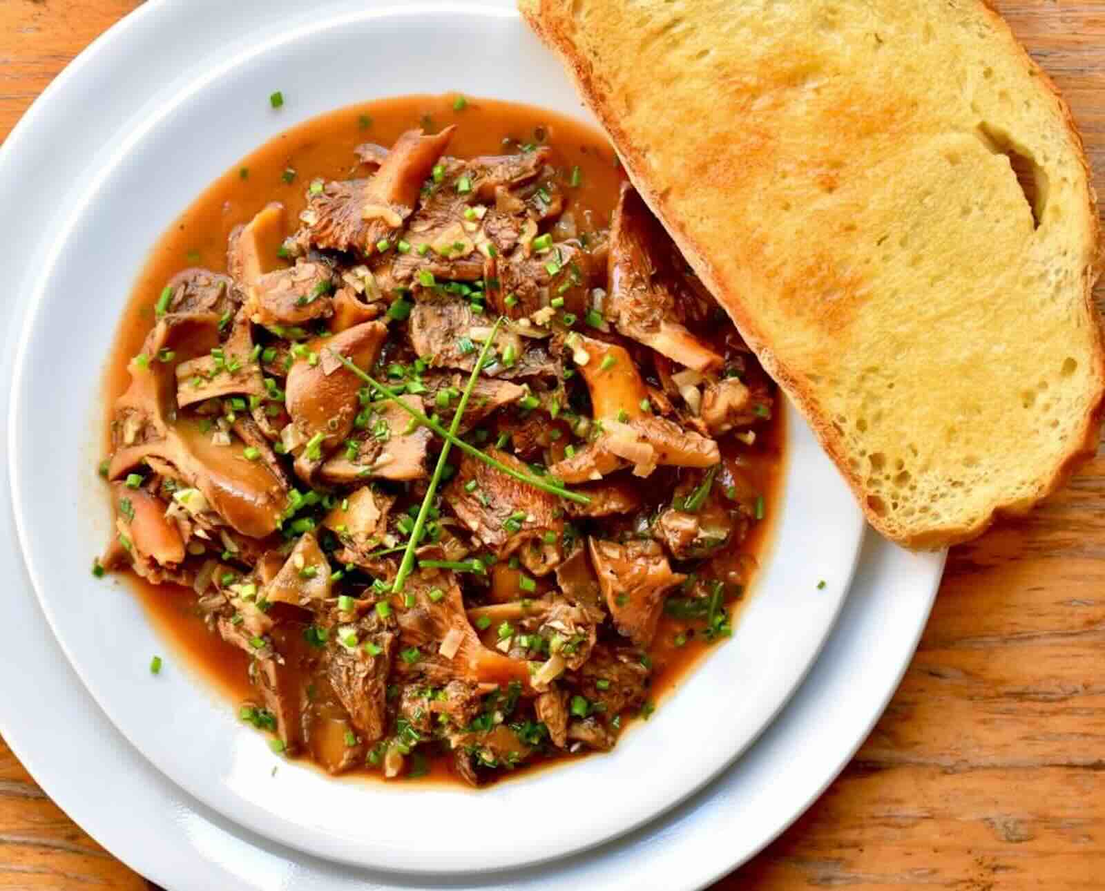A dish of mushrooms in a brown broth served with a toasted slice of bread