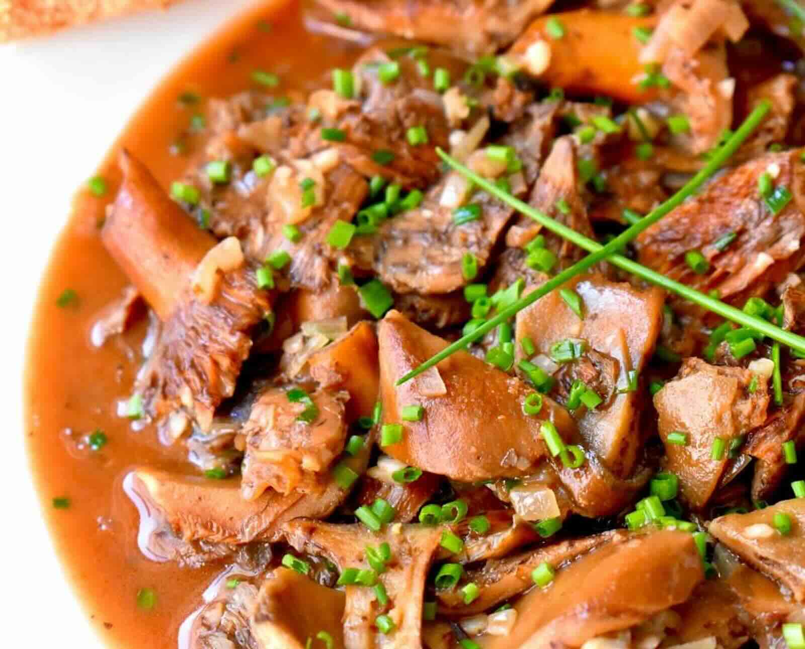 A close-up view of a dish of mushrooms in a brown broth topped with chives