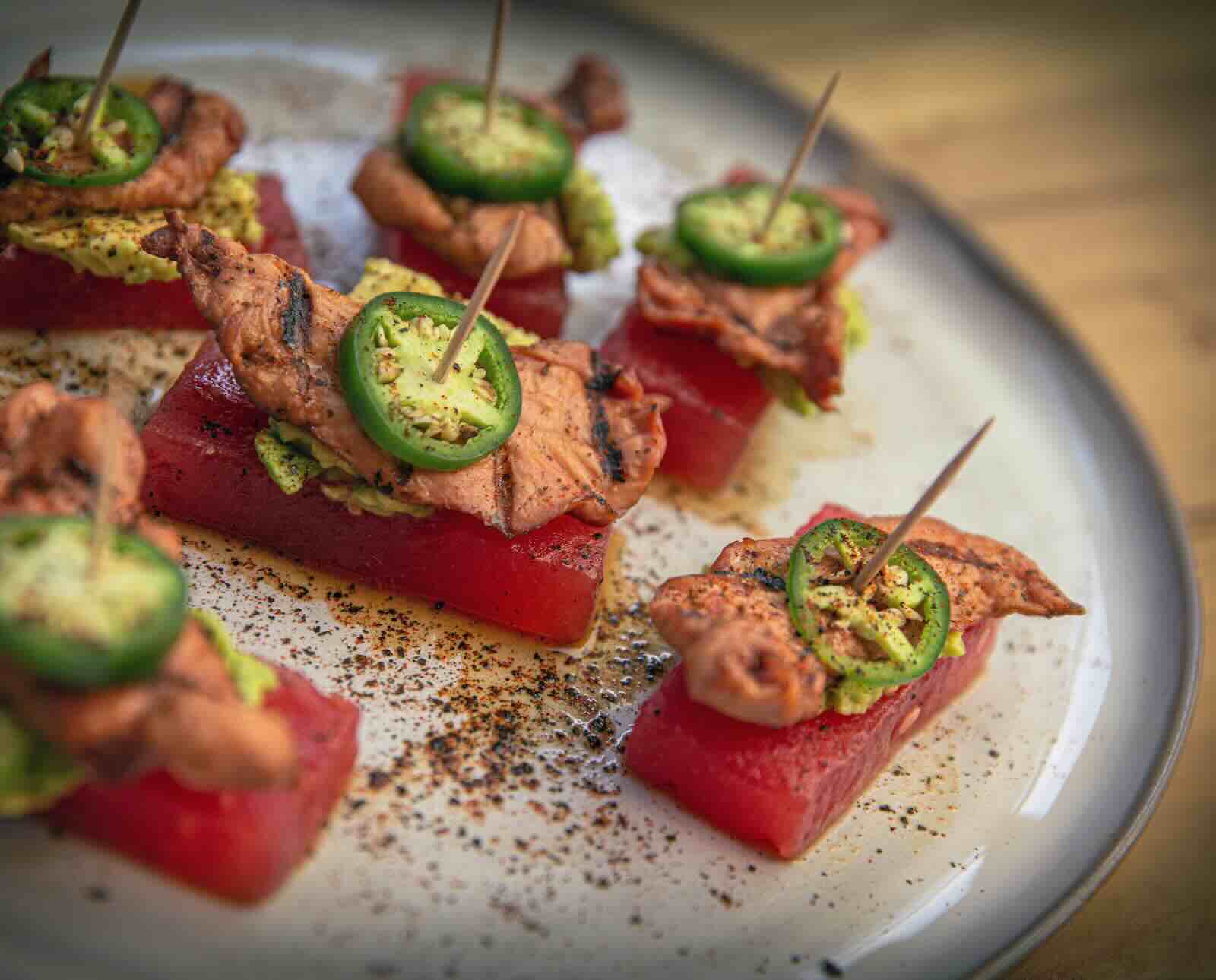 An appetizer dish of watermelon, pheasant, and jalapeno on toothpicks served on a platter