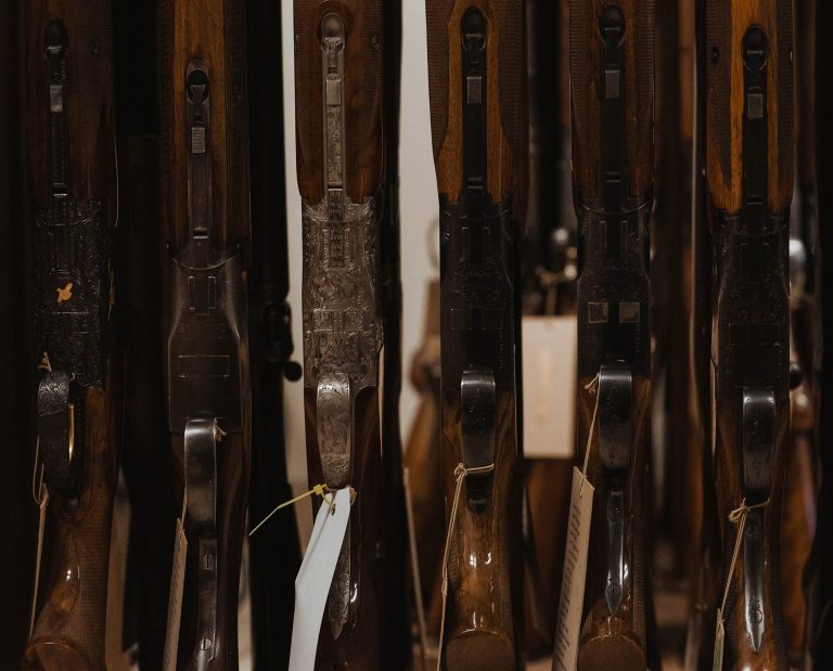 A set of over and under shotguns rest side by side on a store rack.