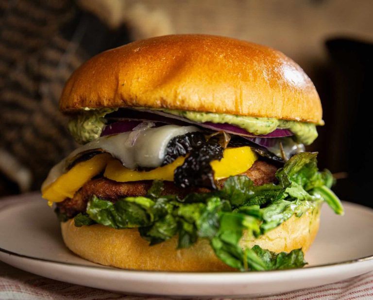 A fresh burger made from wild turkey meat and topped with mango, smokey mayo, cheese, and toasted greens