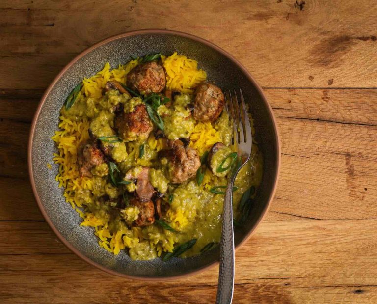 A dish of turkey meatballs served over saffron rice in a creamy poblano sauce on a wooden table background