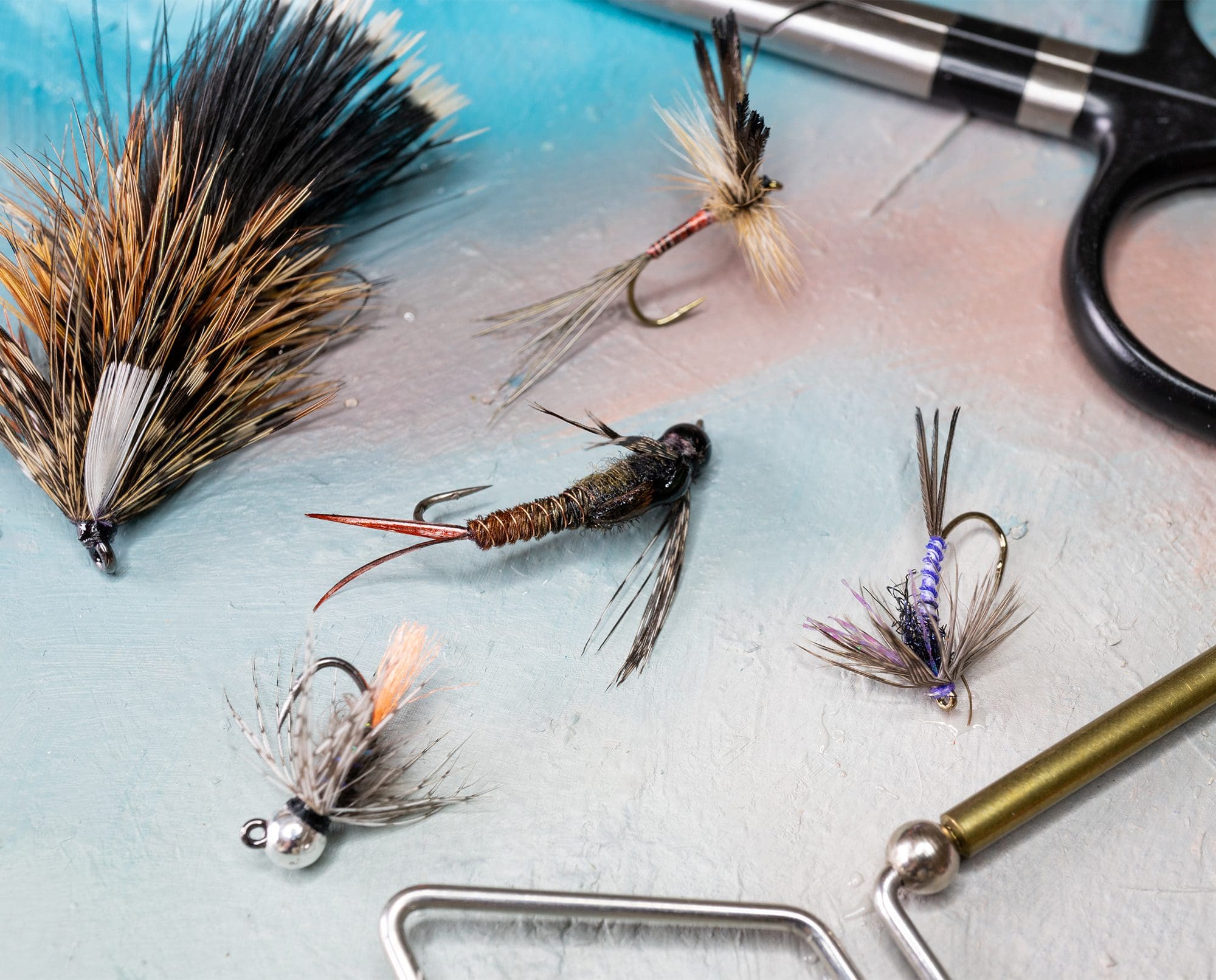 Fly patterns tied with upland bird feathers rest on a table.