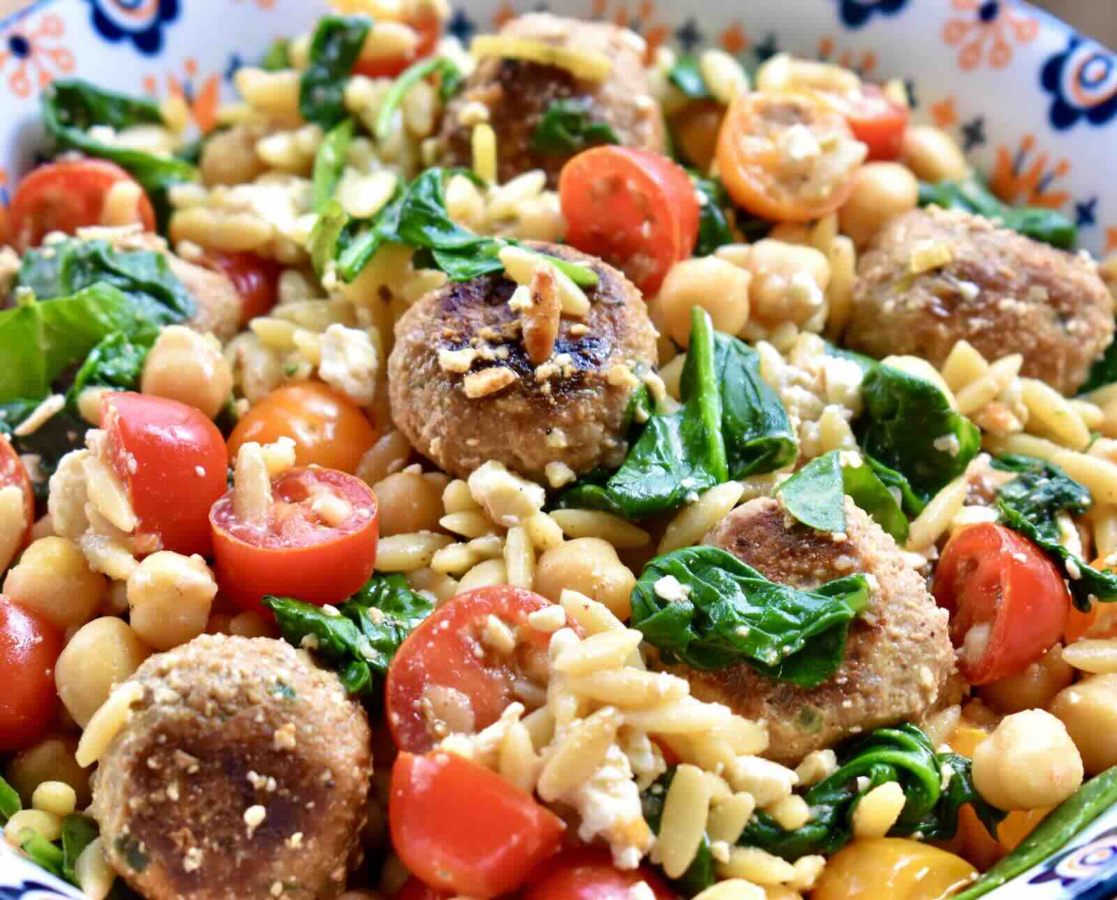 A colorful pasta salad with turkey meatballs, tomatoes, chickpeas, spinach, and orzo pasta.