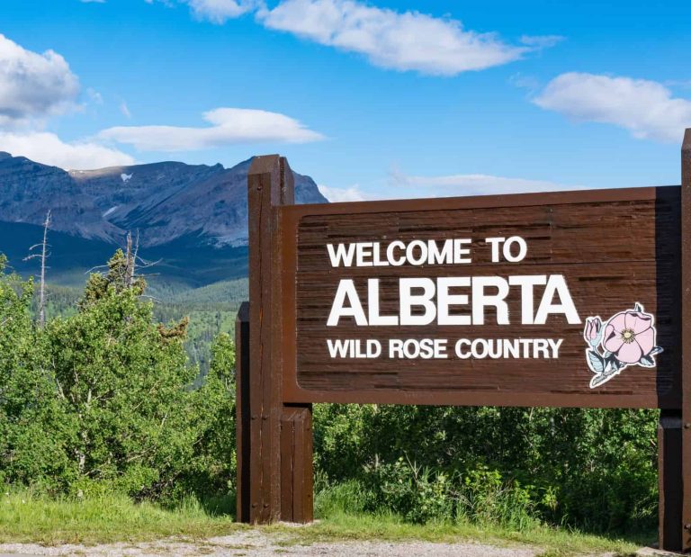 A sign that says "welcome to Alberta" along a road winding through mountains in Canada.