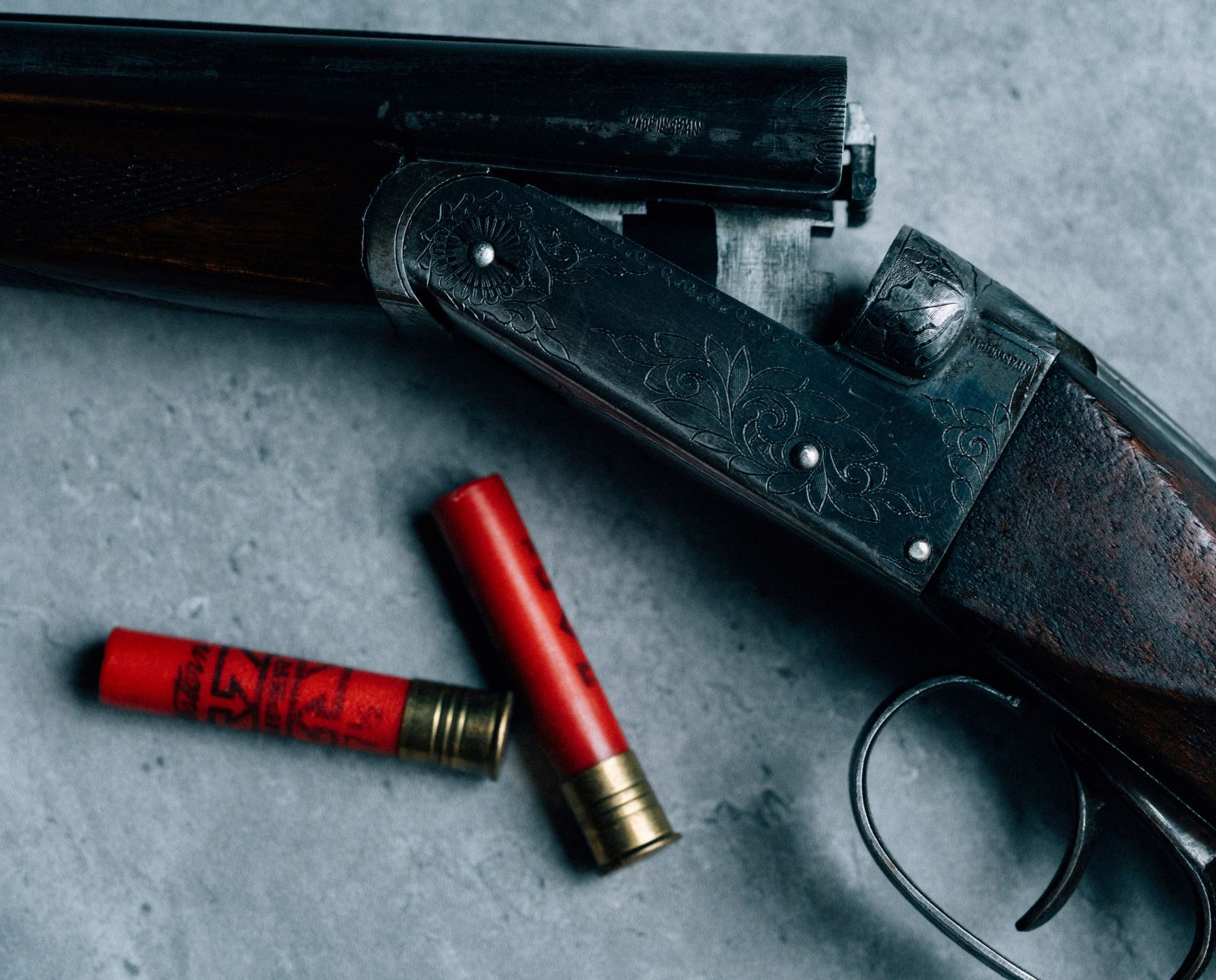 A broken-open .410 shotgun with a wooden stock next to two rounds of ammunition.