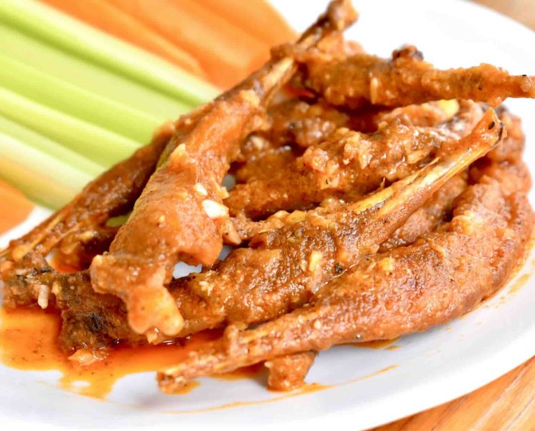 Grouse legs are battered, fried, and smothered in orange buffalo sauce, then served on a white plate with carrot and celery sticks