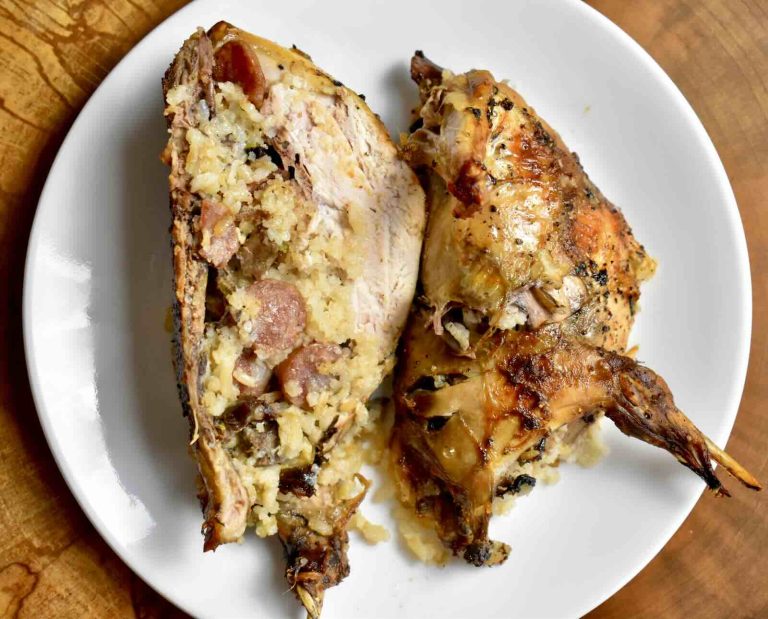 A roasted, whole ruffed grouse stuffed with sticky rice, sliced in half and served on a white plate on a wooden background
