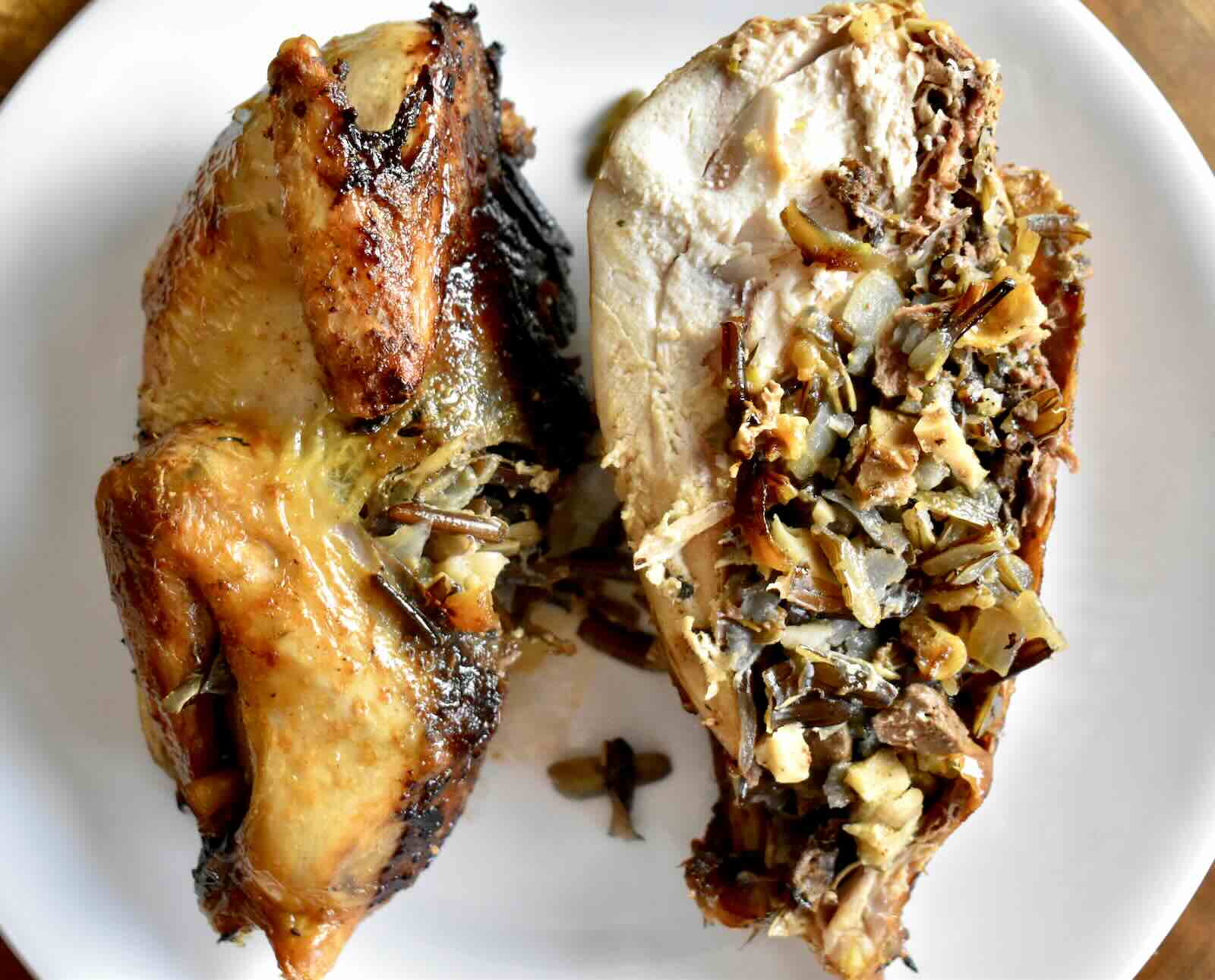 A whole, roasted grouse split in half to show the wild rice and mushroom filling, served on a white plate