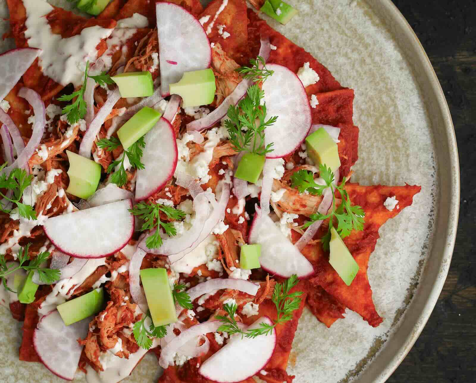 A platter of pheasant chilaquiles served with radishes, avocado, cilantro, and onions