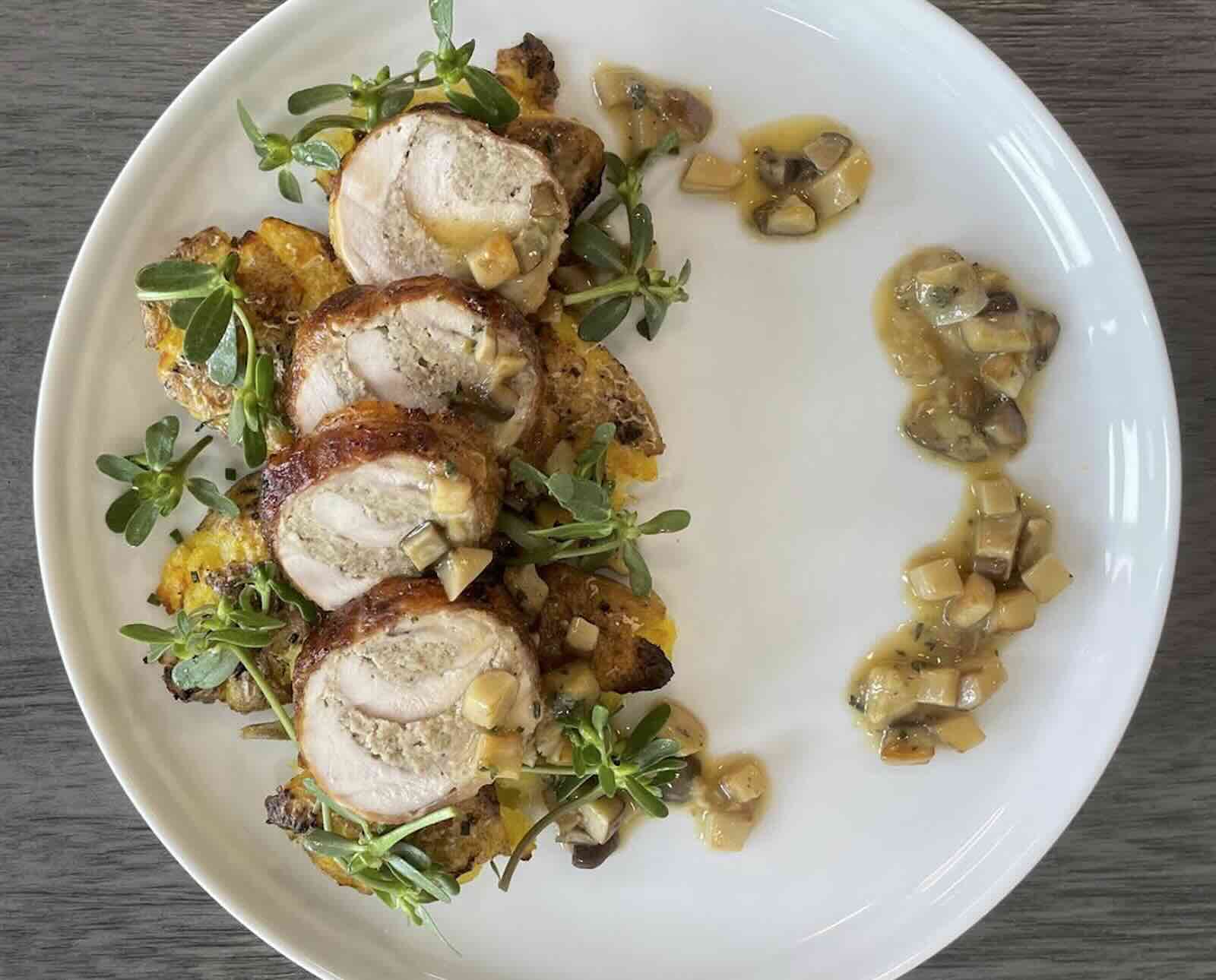 Sliced, roasted chukar served on a white plate with a purslane garnish and a mushroom sauce