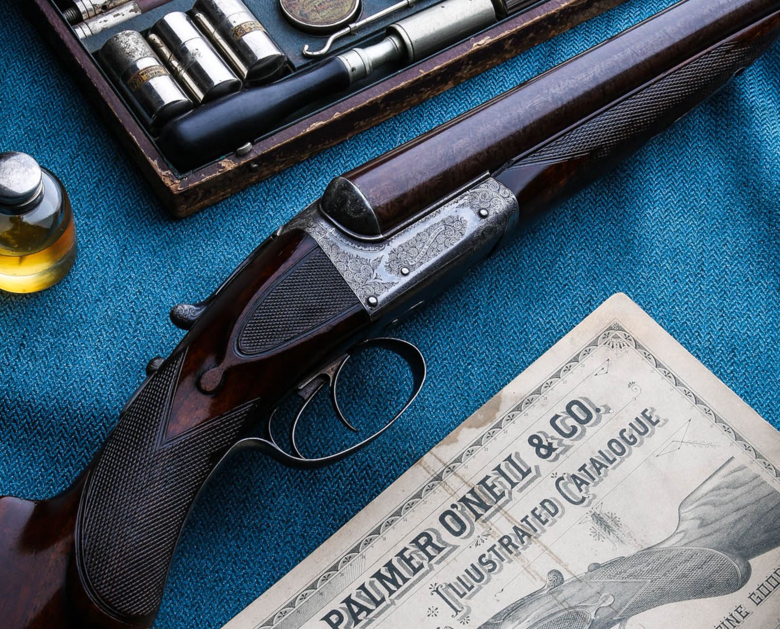 An English Westley-Richards side-by-side shotgun next to original chokes and a vintage advertisement.