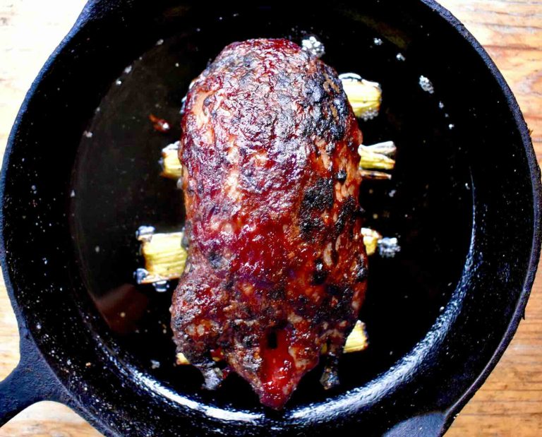 A roasted duck with a crispy skin sits atop celery stalks in a cast iron frying pan
