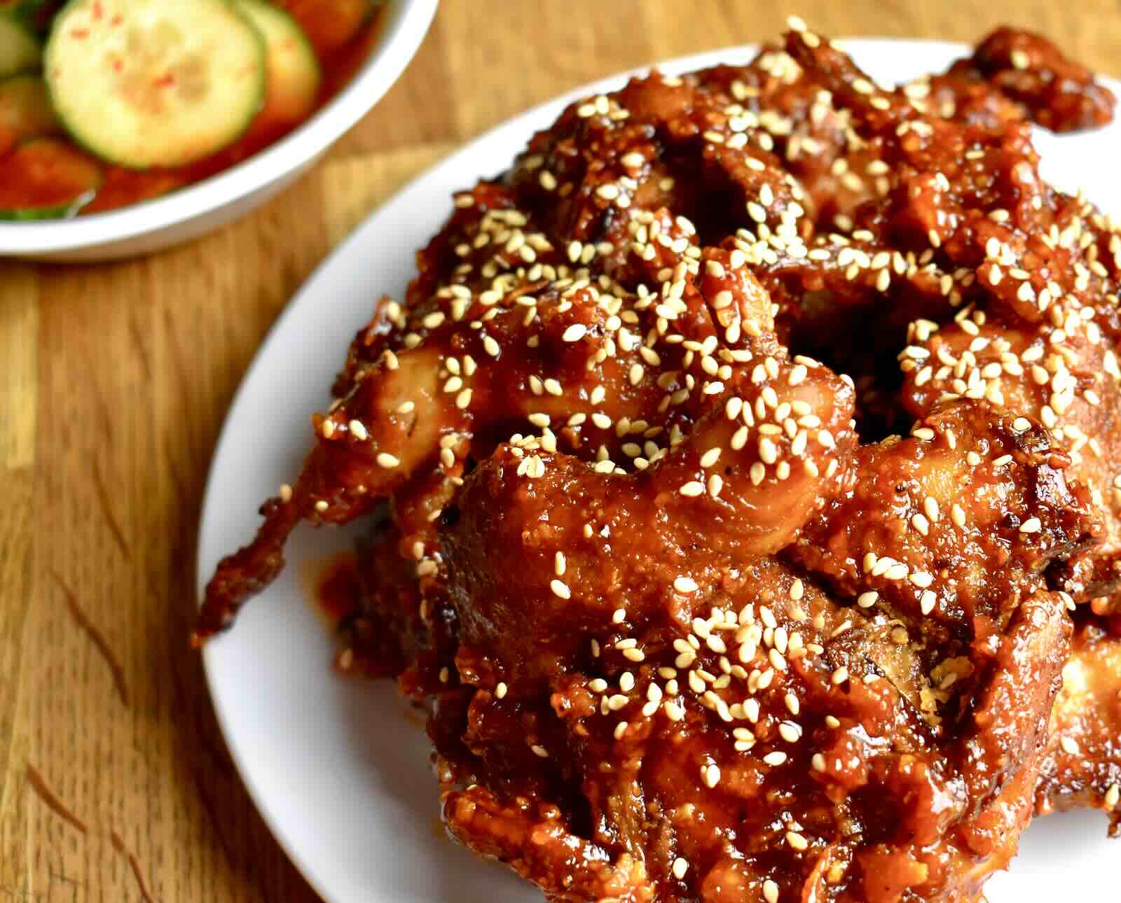 A plate of fried quail tossed in a red sauce and topped with sesame seeds