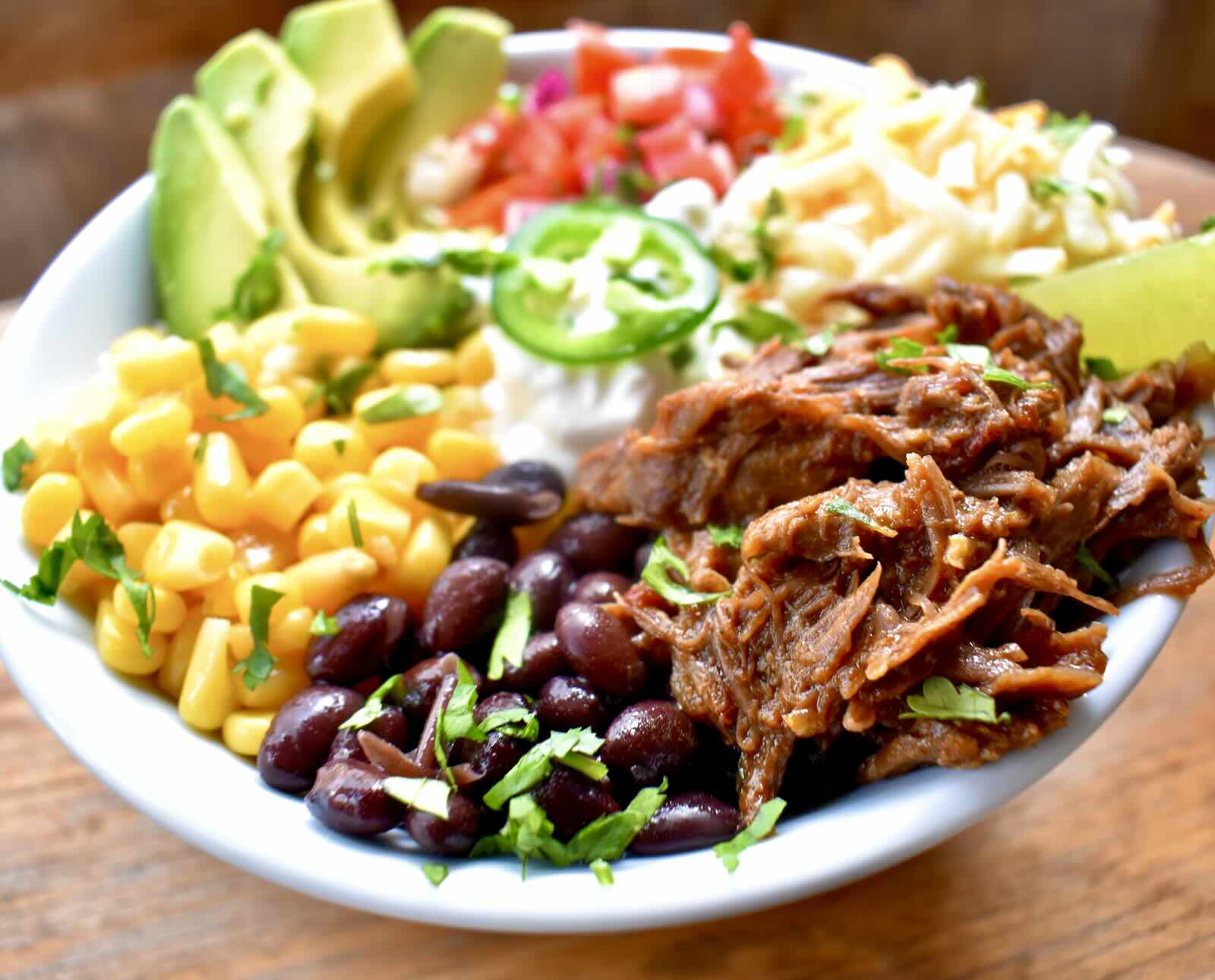 Raccoon barbacoa served with corn, black beans, avocado, tomatoes, cheese, and a lime on top of rice